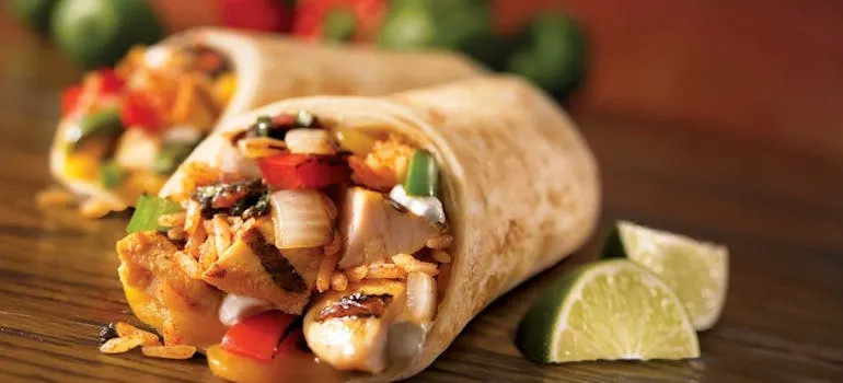 pexels-pixabay-461198.jpg A chicken burrito with vegetables and rice, garnished with lime slices on a wooden surface